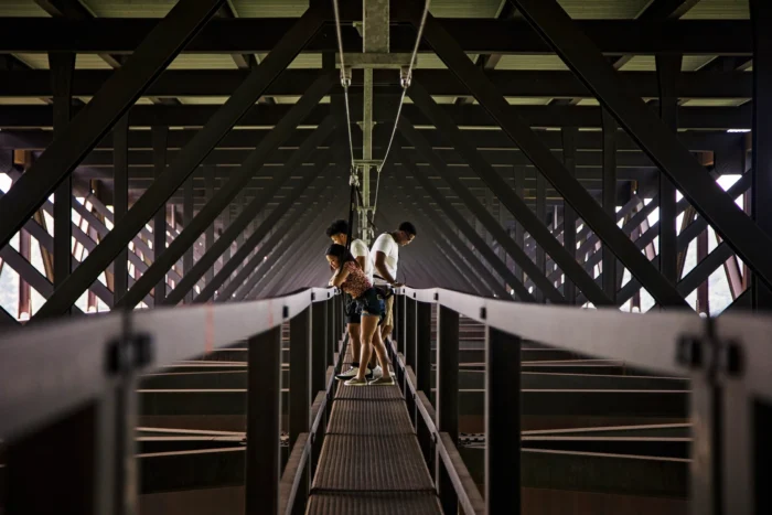 Three people standing on a metal walkway inside the steel truss structure of a bridge. 