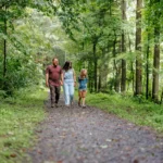 A family of three walking on a gravel path through a lush green forest.