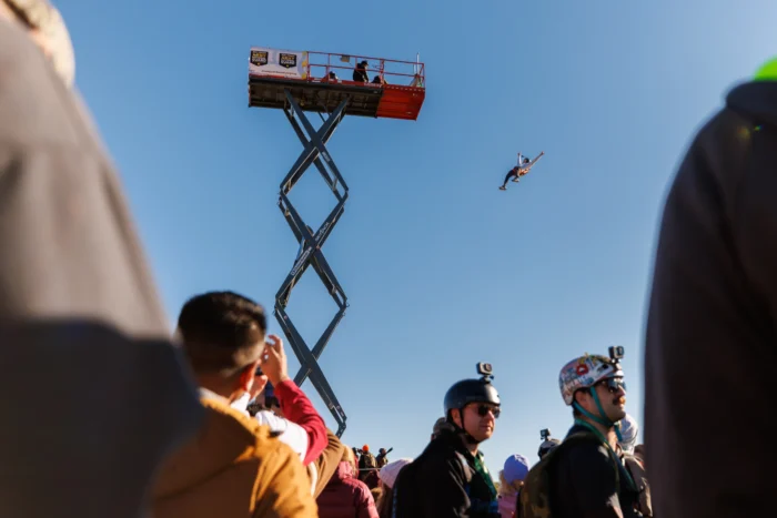 Person BASE jumping from a scissor lift platform while spectators watch from below.