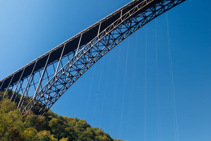 The steel arch New River Gorge Bridge photographed from below with rappel lines featured, against a clear blue sky.