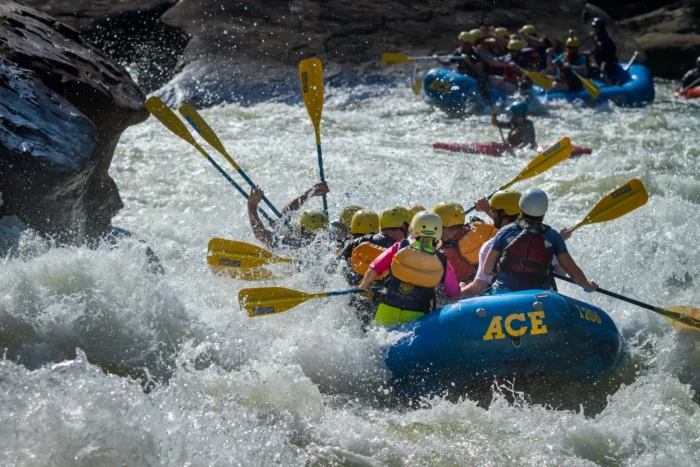 Close-up of whitewater rafters in blue raft getting splashed by turbulent rapids, wearing yellow helmets and life jackets.