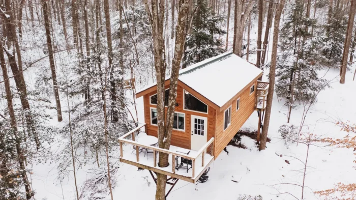 Wooden cabin with snow-covered roof elevated on stilts in a winter forest