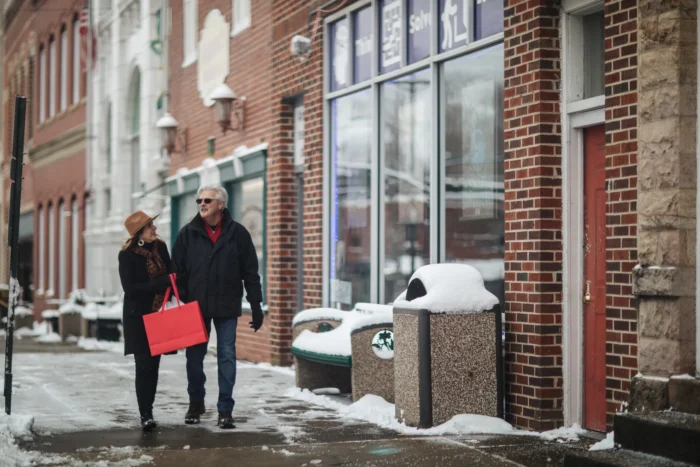 A couple walking on a snowy downtown Fayetteville sidewalk with a shopping bag
