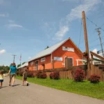 Family walking on the paved White Oak Rail Trail, past an orange freight station building on a sunny day.