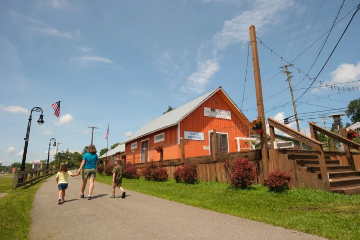 Family walking on the paved White Oak Rail Trail, past an orange freight station building on a sunny day.